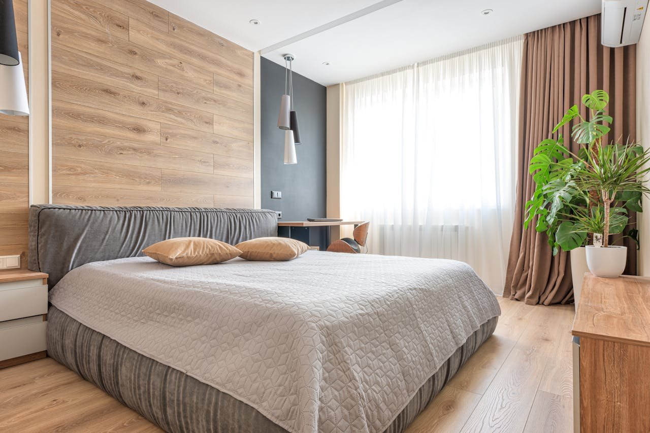 A clean and bright modern bedroom featuring wooden accents, neutral tones, and a potted plant.